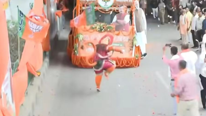 हिंदू देवता हनुमानाचा वेश धारण केलेली आणि भाजपचा झेंडा फडकवणारी एक व्यक्ती लखनौमध्ये भाजपचे नेते नितीन नबिन यांचे स्वागत करत आहे.